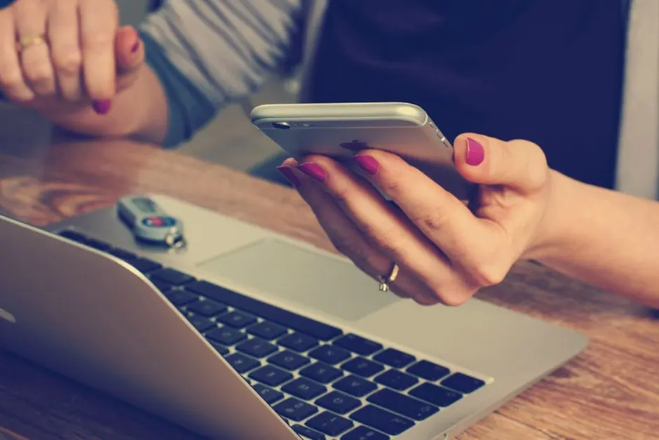 A girl working on a laptop with iPhone in her left hand.